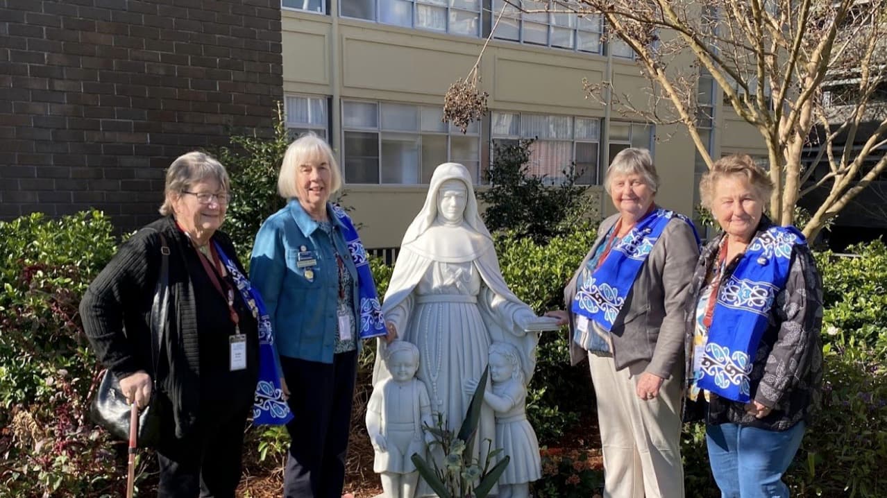 Members wearing blue ceremonial stoles beside a religious statue in a garden