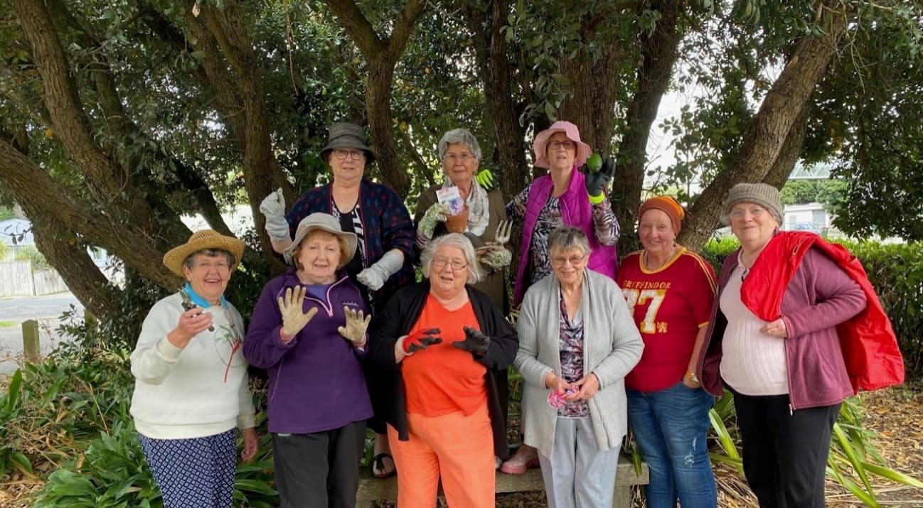 A group of members with gardening gloves gathered under a tree on a community planting day